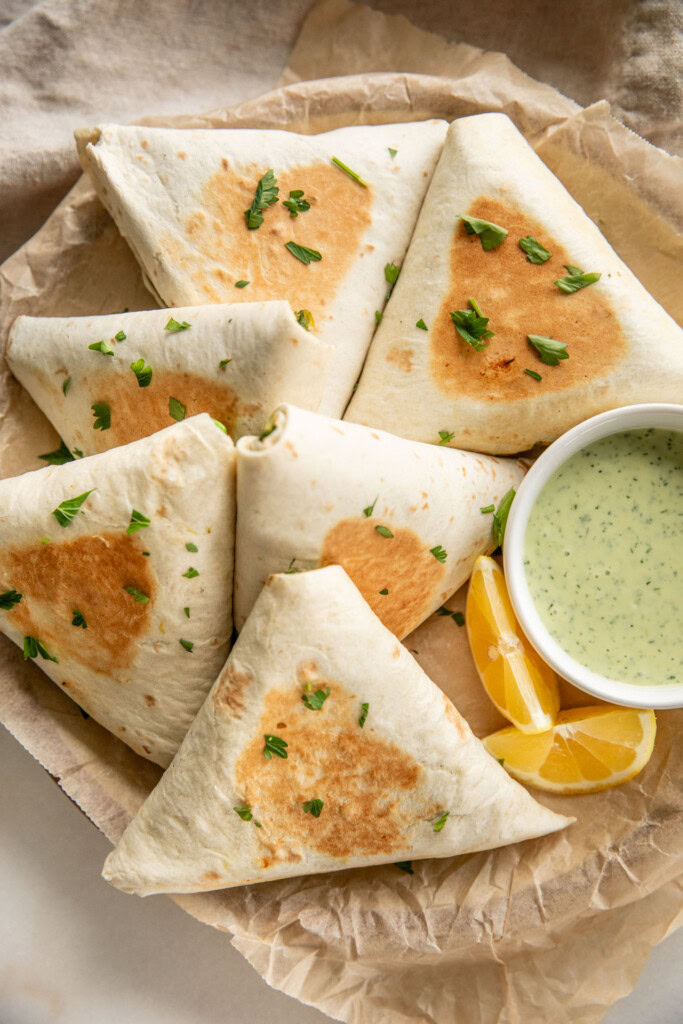 Six toasted wraps on a parchment lined plate served with a small bowl of herby dipping sauce.