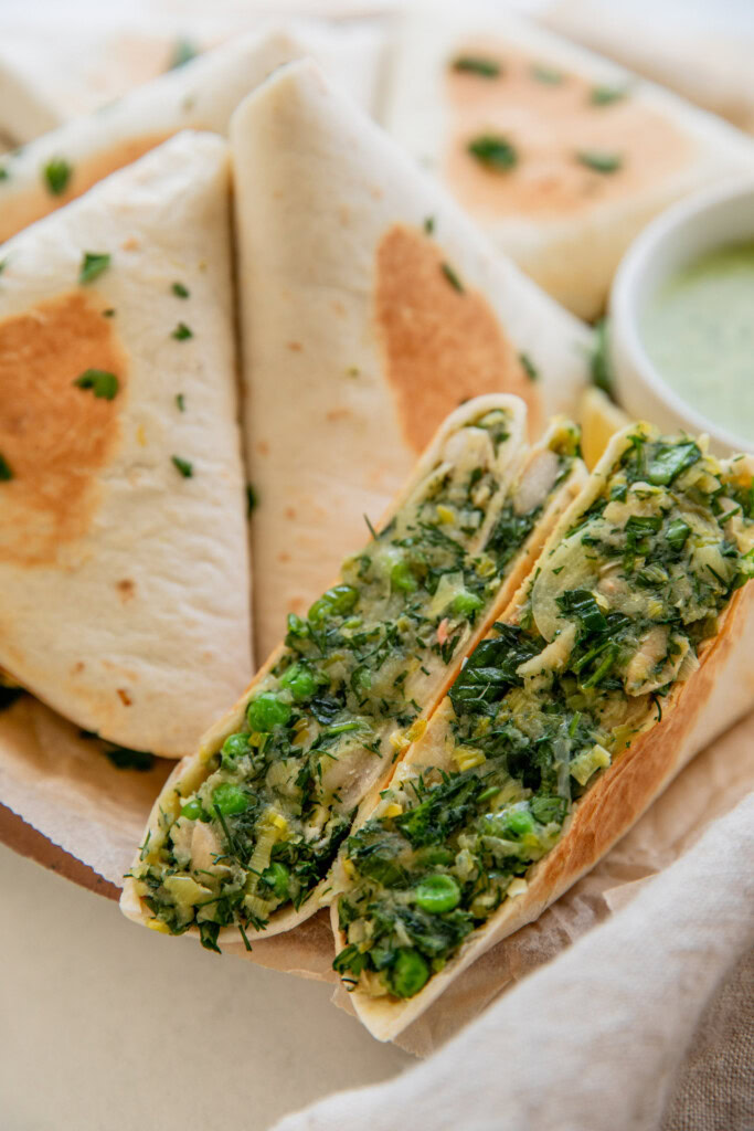 A cut herby potato and leek wrap cut in half and displayed in front of a plate of toasted wraps in the back.