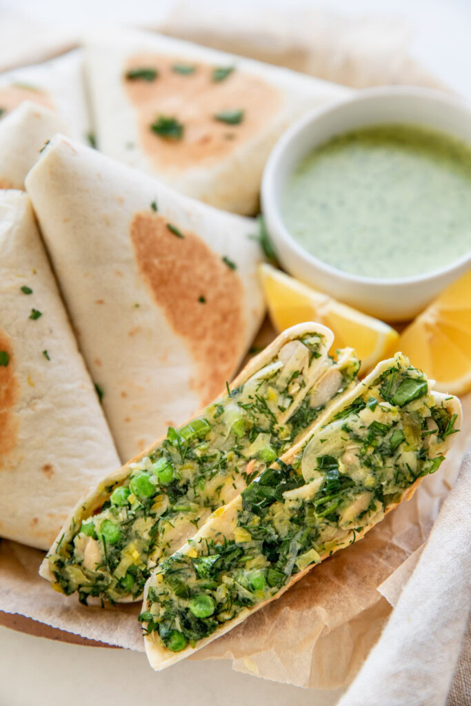 Inside view of a potato leek wrap cut in half in front of a pile of toasted wraps on a plate.