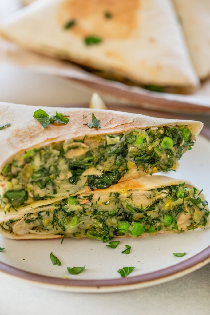 One potato leek wrap cut in half and stacked on a plate to reveal the herby filling.
