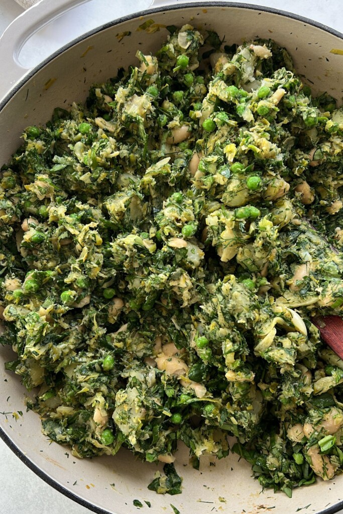 The herbs and greens mixed together with the potato leek filling in a pan.