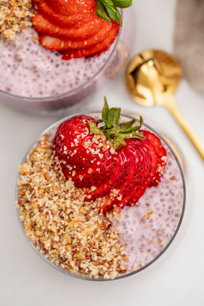 Top down view of two cups filled with chia pudding topped with a date crumble and sliced strawberry.