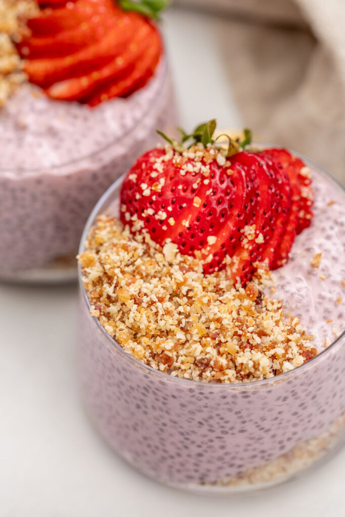 Side view of two cups layered with an almond date crumble and strawberry chia pudding topped with sliced strawberries.