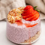 A jar layered with almond date crumble then strawberry chia pudding and topped with strawberry slices.