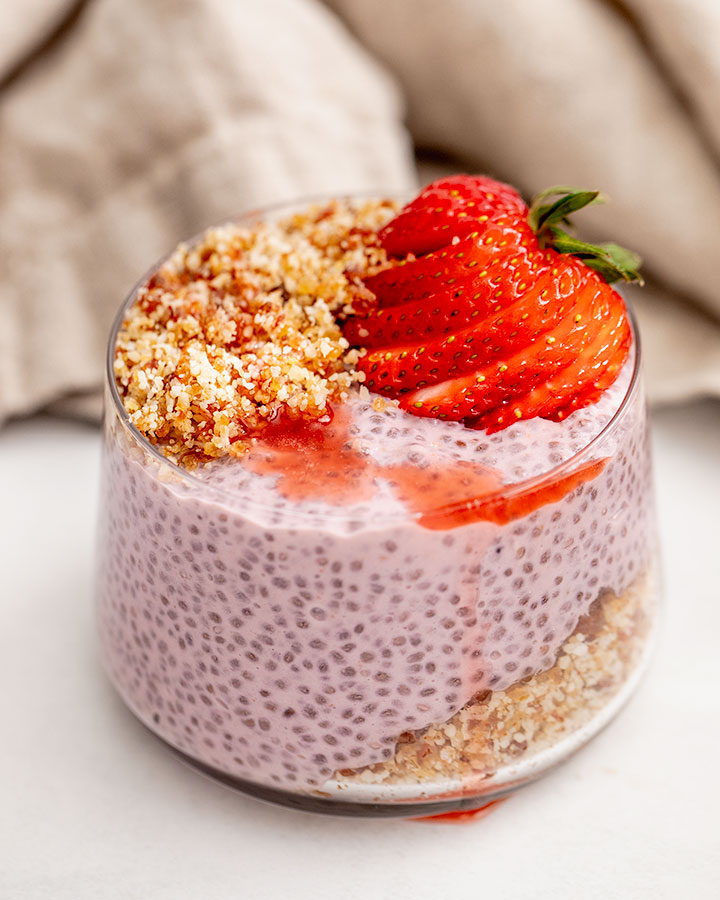 A jar layered with almond date crumble then strawberry chia pudding and topped with strawberry slices.