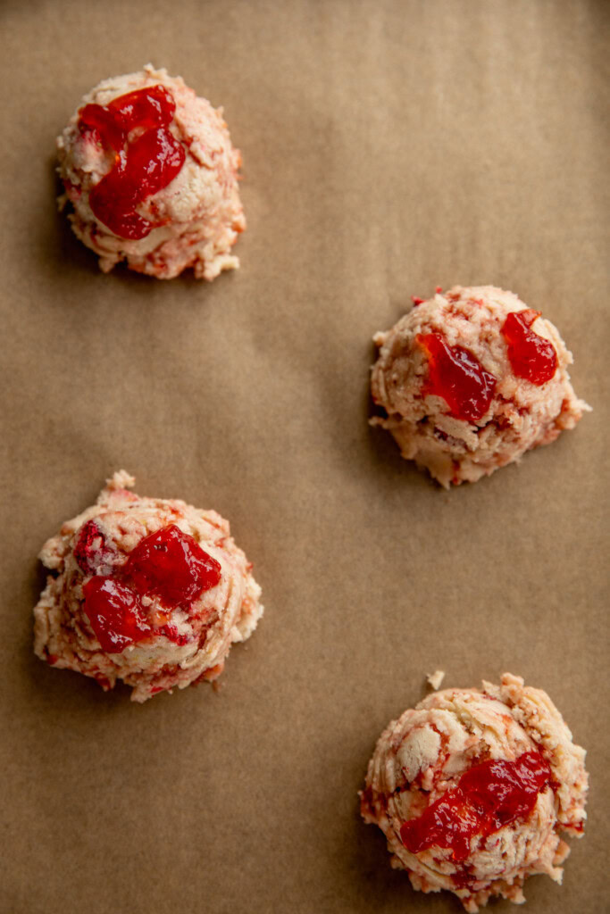 Cookie dough balls on a baking sheet topped with extra dollops of jam on top.