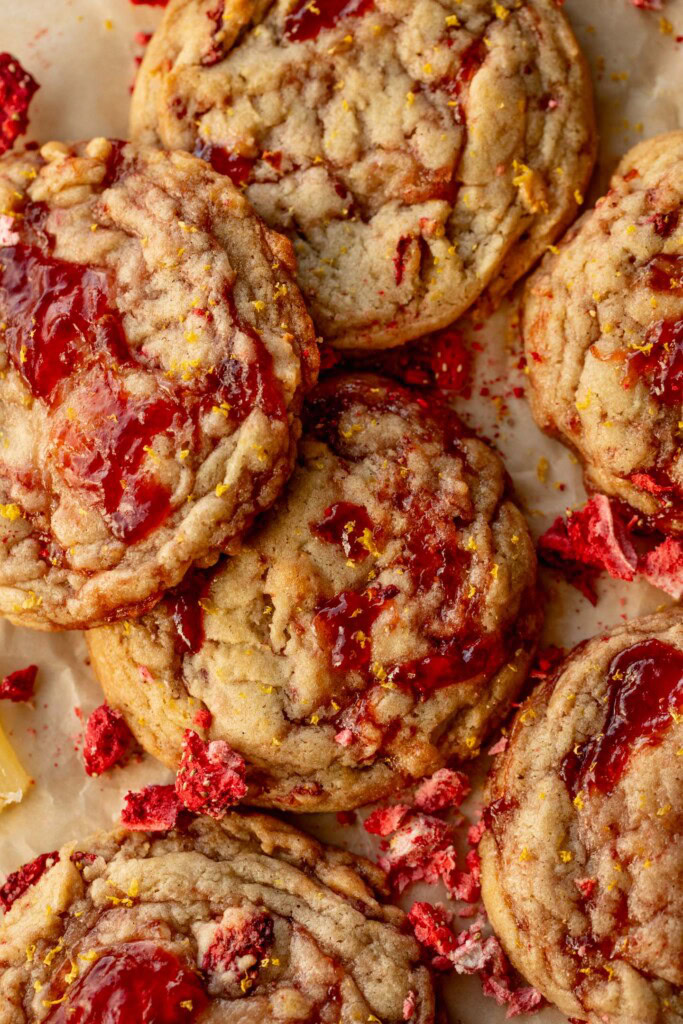 Large batch of cookies spread out over a piece of parchment paper covered in crushed freeze-dried strawberries.