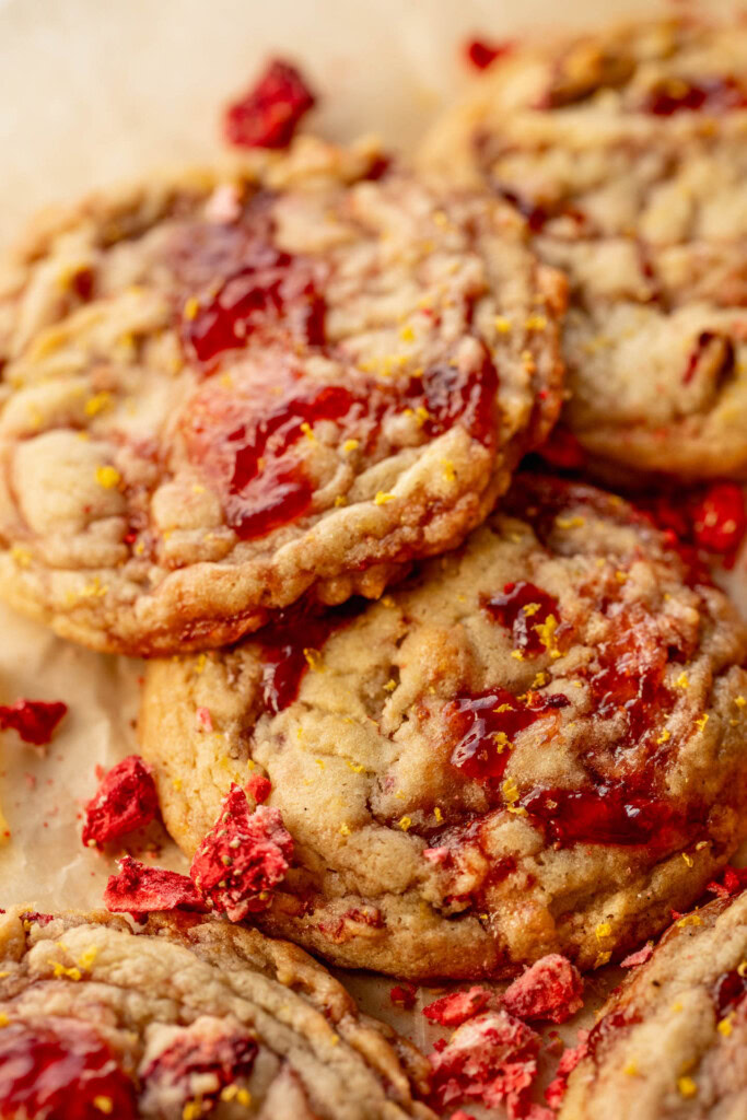 Close up of 3 strawberry jam cookies on a piece of parchment paper.