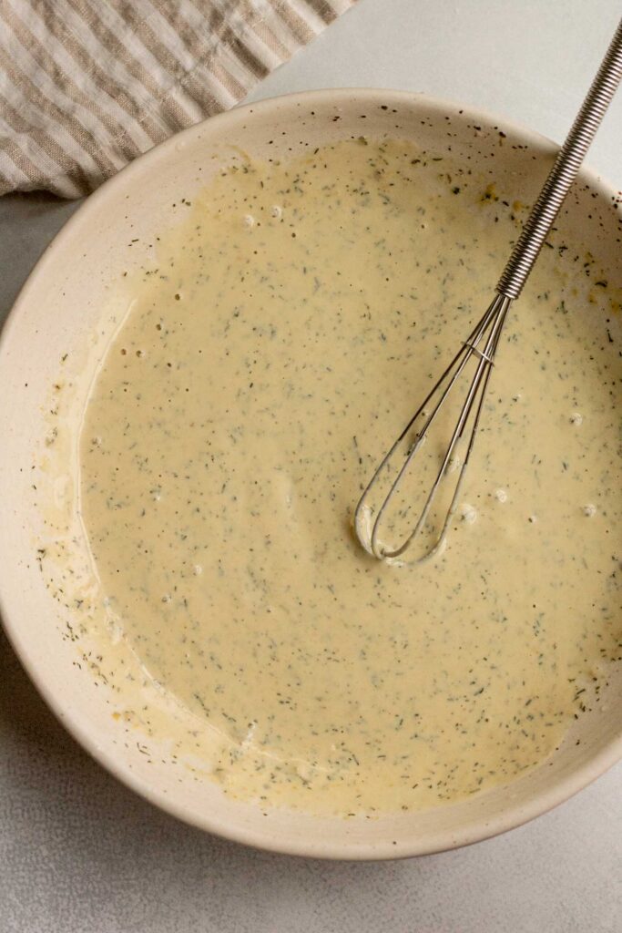 Mixing the tahini ranch together in a bowl with a baby whisk.