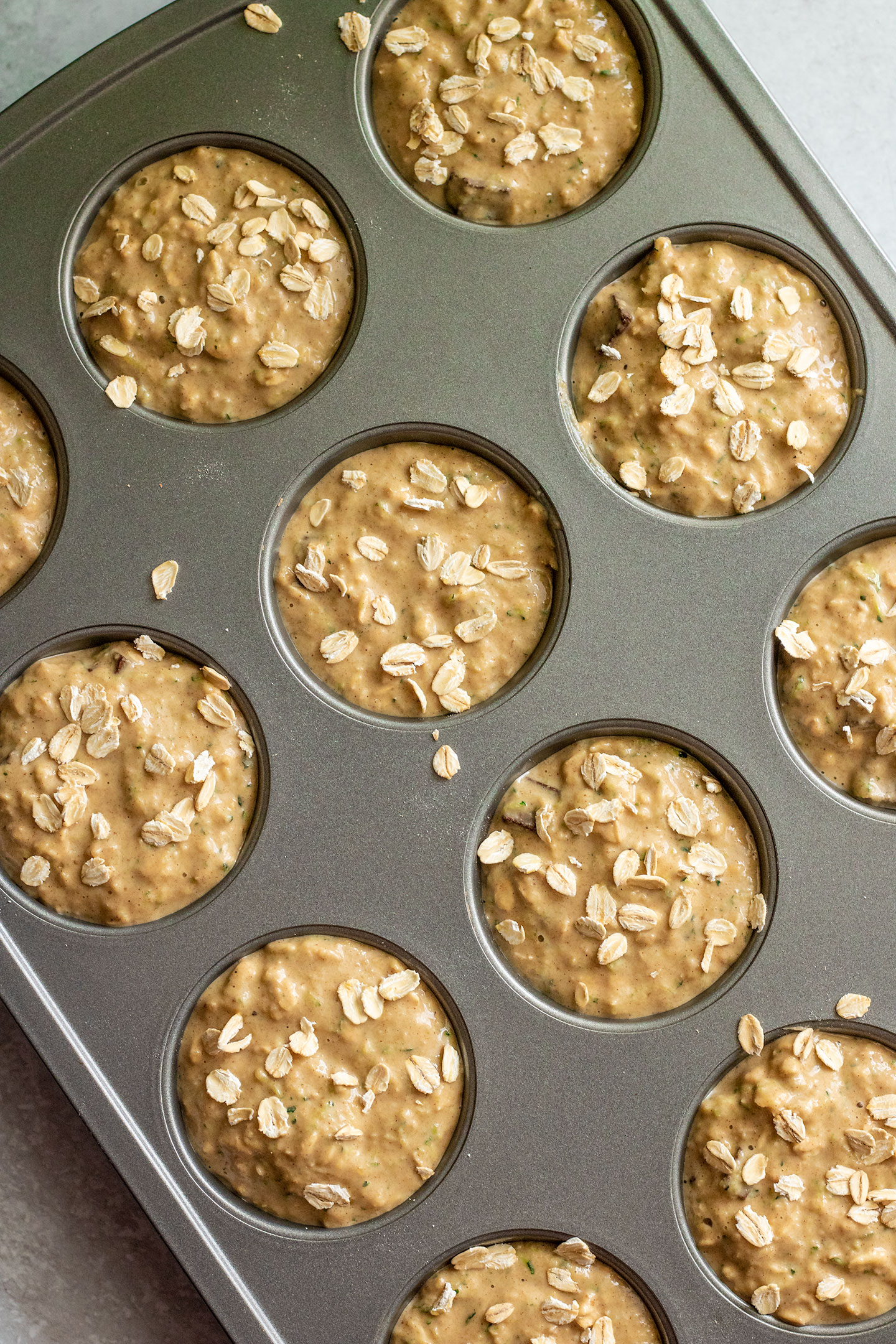 Adding the muffin batter to a muffin tin, muffins decorated with extra oats sprinkled on top.